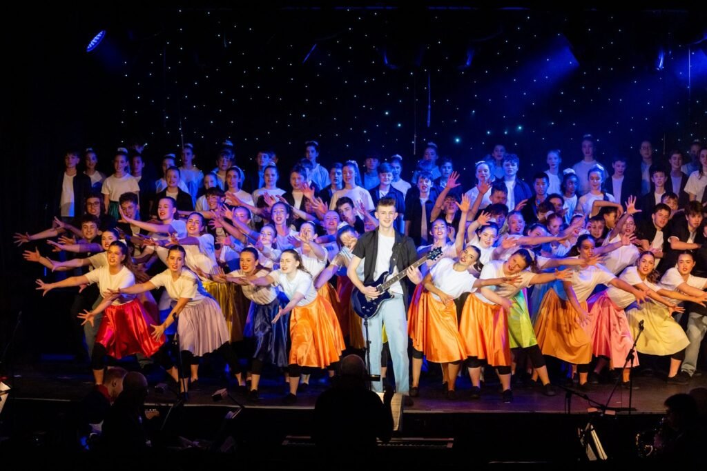 Harpenden Gang Show full cast singing with a guitarist