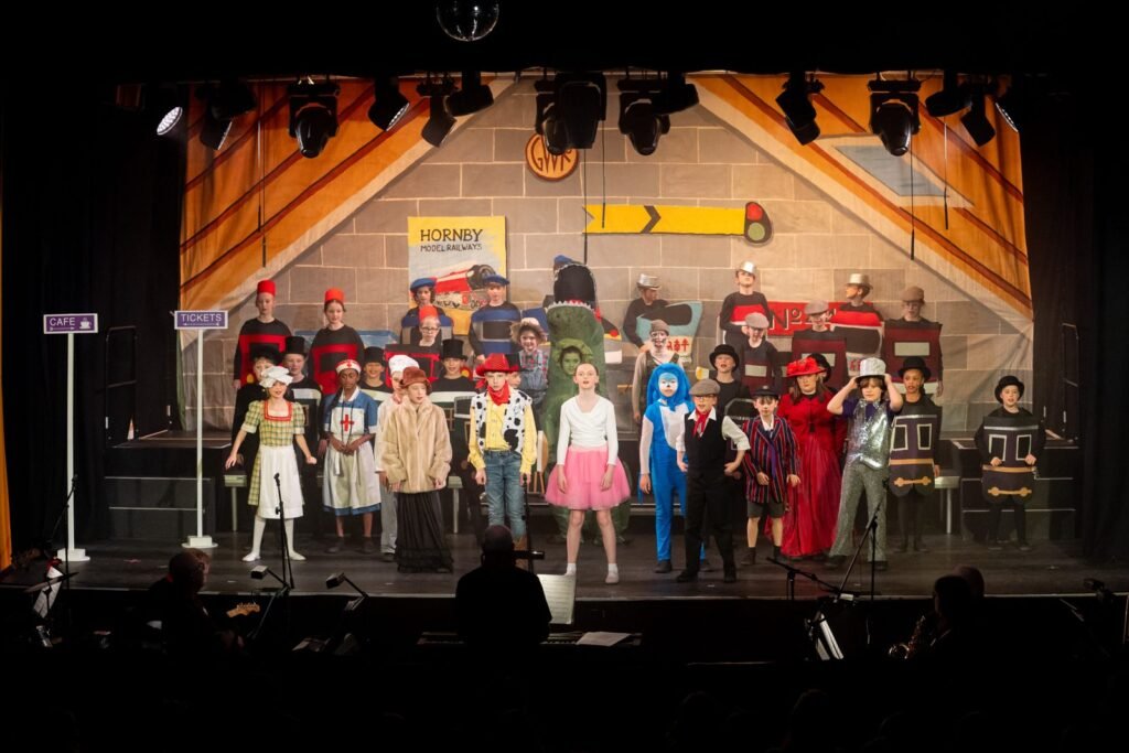 Harpenden Gang Show cast in a railway station scene