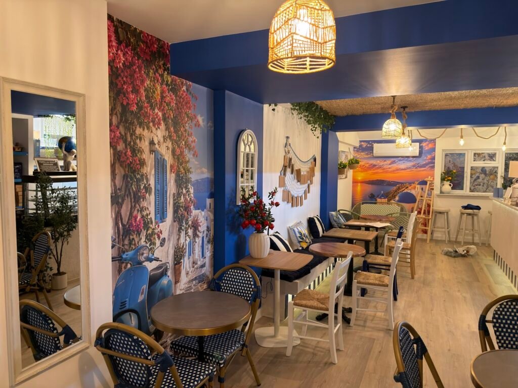Inside Kalimera Greek Bakery Café on Leyton Road, Harpenden, with blue and white Greek décor and a bougainvillea mural